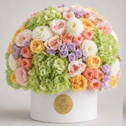 Round bouquet of pastel roses, hydrangeas, and white blooms in a white box