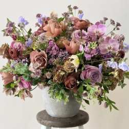 A mixed bouquet of pink, lavender, and peach flowers in a gray vase.