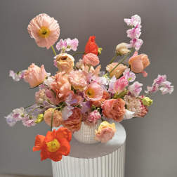 Loose bouquet of peach, pink, and coral flowers in a white vase