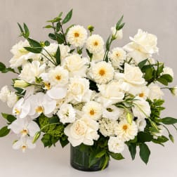 White floral arrangement in a dark glass vase with orchids and roses