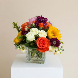 Mixed bouquet of roses, sunflowers, and purple daisies in a glass vase