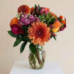 Colorful mixed bouquet in a clear glass vase with orange and purple blooms