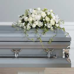 White floral casket spray with trailing greenery on a gray casket