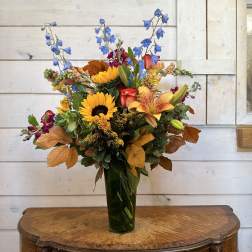 Mixed bouquet with sunflowers, lilies, and blue delphinium in a tall vase