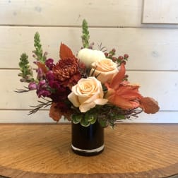 Peach roses and burgundy flowers arranged in a black vase