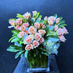 Peach roses and blue hydrangeas in a clear square vase