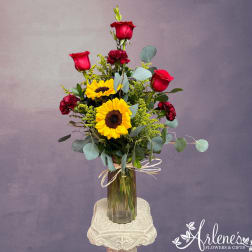 Tall bouquet of red roses and yellow sunflowers in a glass vase