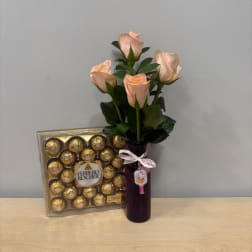 Peach roses in a purple vase beside a box of Ferrero Rocher chocolates