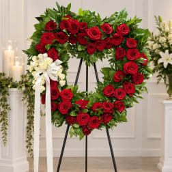 Heart-shaped wreath of red roses with a white ribbon bow on an easel