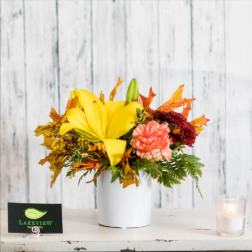 Yellow lily and carnations in a white vase with autumn leaves