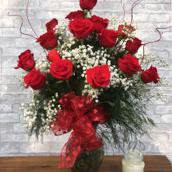 Red roses arranged in a glass vase with baby's breath and a red ribbon