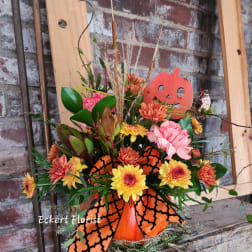 Orange and yellow floral arrangement in a pumpkin container with a Halloween decoration