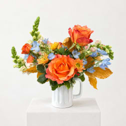 Orange and blue mixed bouquet in a white mug vase