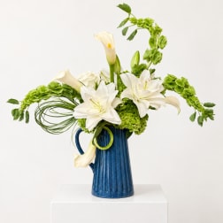 White lilies and green flowers in a blue pitcher vase