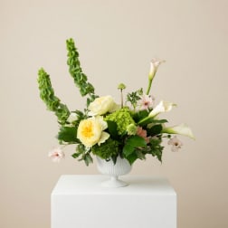 White and pale yellow floral arrangement in a white pedestal vase