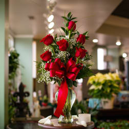 Red roses arranged in a clear glass vase with a red ribbon