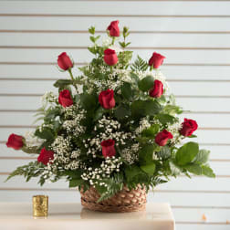 Basket arrangement of red roses and white filler flowers in a woven basket.