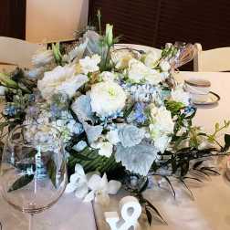 Low centerpiece of white and pale blue flowers on a table