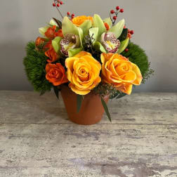 Orange and yellow roses in a terracotta pot with red berry accents