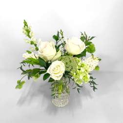 White roses arranged in a clear glass vase with green accents