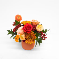 Orange and red mixed flower arrangement in a round orange vase