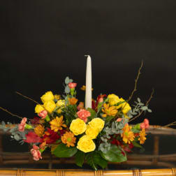 Yellow and pink floral arrangement with a white taper candle