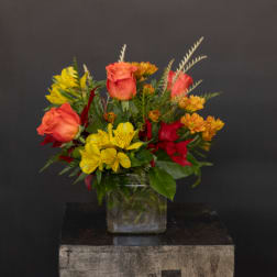 Mixed bouquet of orange roses and yellow flowers in a glass vase