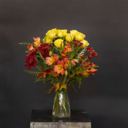 Yellow roses and red-orange flowers in a clear glass vase