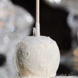 White candy apple on a stick coated in fine powder against a soft, sparkling background