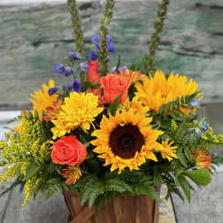 Basket arrangement with sunflowers, coral roses, and purple flowers