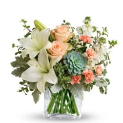 Bouquet of white lilies, peach roses, and blue-green blooms in a clear vase
