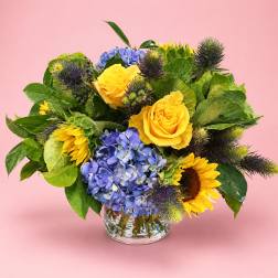 Yellow roses and blue hydrangeas in a clear glass vase