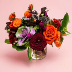 Orange and burgundy flower arrangement in a clear glass vase