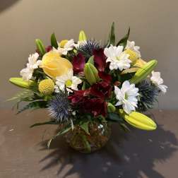 Bouquet of yellow roses, white daisies, and burgundy flowers in a glass vase