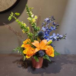 Orange lilies and roses in a brown vase with blue flowers