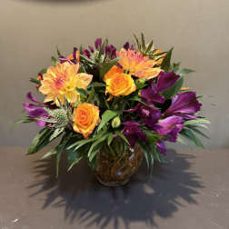 Orange roses and purple flowers arranged in a glass vase