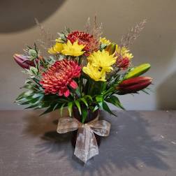 Bouquet of red and yellow flowers in a dark vase with a sheer bow