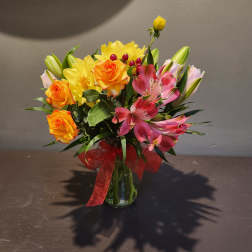 Mixed bouquet of orange roses, yellow daisies, and pink lilies in a glass vase