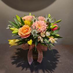 Mixed bouquet in a dark vase with pink, peach, and yellow flowers