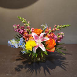 Colorful bouquet with orange roses, a white lily, and blue flowers in a glass vase