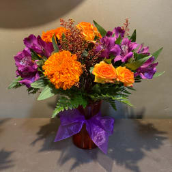 Orange and purple mixed bouquet in a vase with a purple ribbon