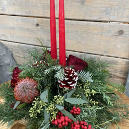 Holiday centerpiece with red candles, roses, pinecones, and evergreen branches