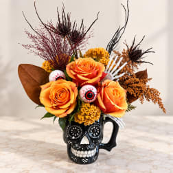 Orange roses arranged in a black skull mug with Halloween accents