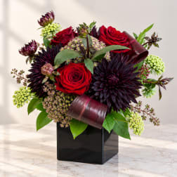 Red roses and dark purple flowers in a black square vase