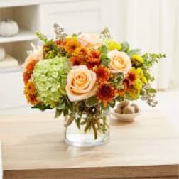 Peach roses and mixed autumn flowers in a clear glass vase