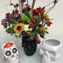 Floral arrangement in a black skull vase with colorful skull planters beside it