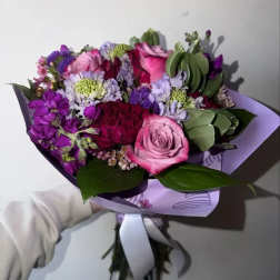Handheld bouquet of pink and purple flowers wrapped in lavender paper