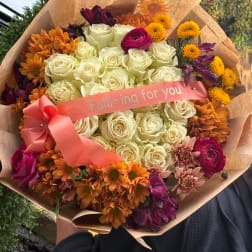 Bouquet of cream roses with orange and purple flowers, wrapped with a pink ribbon