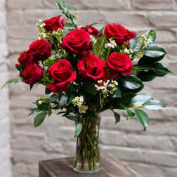Red roses arranged in a clear glass vase with small white filler flowers