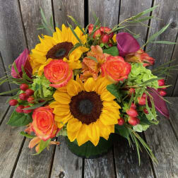 Bouquet of sunflowers, orange roses, and purple calla lilies in a vase